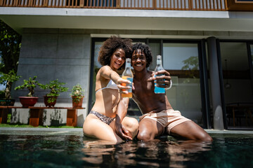 Young couple of African descent enjoying a sunny day at a luxurious pool. They are sitting at the...