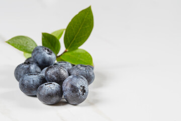 Ahandful of plump fresh blueberries with a sprig of blueberry leaves on a white marble background