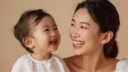 Heartwarming studio image of an Asian mother gazing lovingly at her joyful baby, reflecting their deep emotional bond.