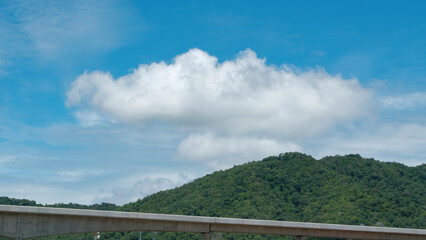 Serene landscape with a cloudy sky over green hills and a concrete bridge.