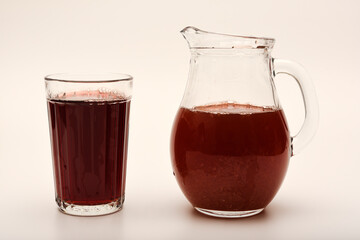 Cherry nectar in a jug and a glass on a white background.