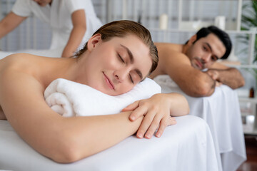 Caucasian couple customer enjoying relaxing anti-stress spa massage and pampering with beauty skin recreation leisure in day light ambient salon spa at luxury resort or hotel. Quiescent