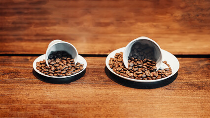 Two ceramic cups spill roasted coffee beans on wooden surface, showcasing rich texture and color of beans