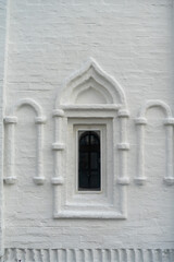 A window in the white wall of an ancient temple or building. A window on a white brick wall.