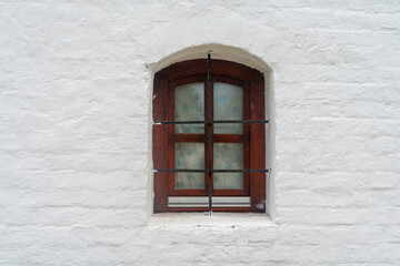 A window in the white wall of an ancient temple or building. A window on a white brick wall.