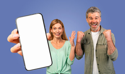 This image features a couple, a man and a woman, excitedly holding a smartphone with a blank white screen. They are both smiling and looking at the camera. The background is a solid blue color.