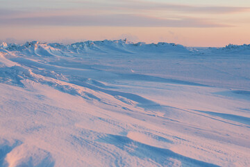 Winter arctic landscape. Cold frosty winter weather. Harsh polar climate. Ice hummocks on the frozen sea in the Arctic. View of snow and ice at sunset. Picturesque nature of the Arctic. Far North.
