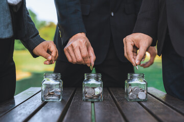 Business people put coin to money saving glass jar on outdoor table as sustainable money growth investment or eco-subsidize. Green corporate promot and invest in environmental awareness. Gyre