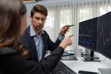 Two business traders discussing on dynamic stock market in currency rate investment trading on two pc screens with compare real time graph on risk or profit point of data at modern office. Postulate.