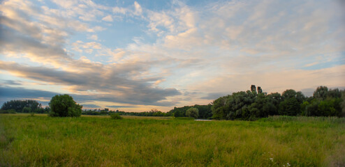 Natural Sunset Sunrise Over a forest or meadow. Bright beautiful sky and dark earth. Small clouds.