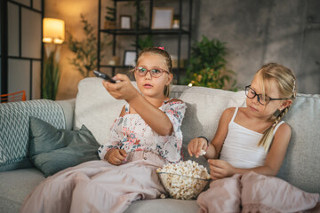 Two young girls child sit on sofa watch movie and eat popcorn