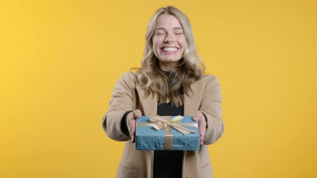 Happy young businesswoman gift box on yellow background. Student girl smiling, giving present to camera. Offer surprise for you.