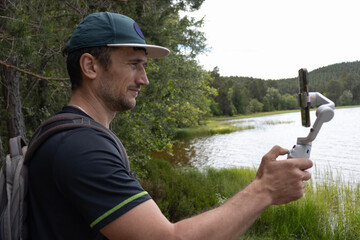 European man shoots video with mobile phone on stabilizer. Young athletic man walks and takes photos.