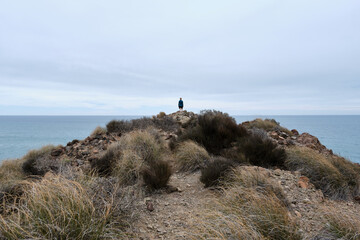Woman with outstretched arms on a cliff, contemplating the sea.