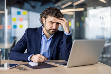 Businessman experiencing stress working on laptop in office. Professional looks frustrated and...