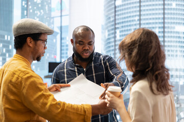 Real estate advisor discussing a promising property deal with potential corporate clients, examining the blueprints and planning the architectural layout of a modern office space. Consider renting.