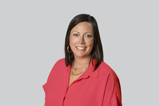 Headshot of Caucasian brunette middle age business woman in studio on gray backdrop with a red shirt on