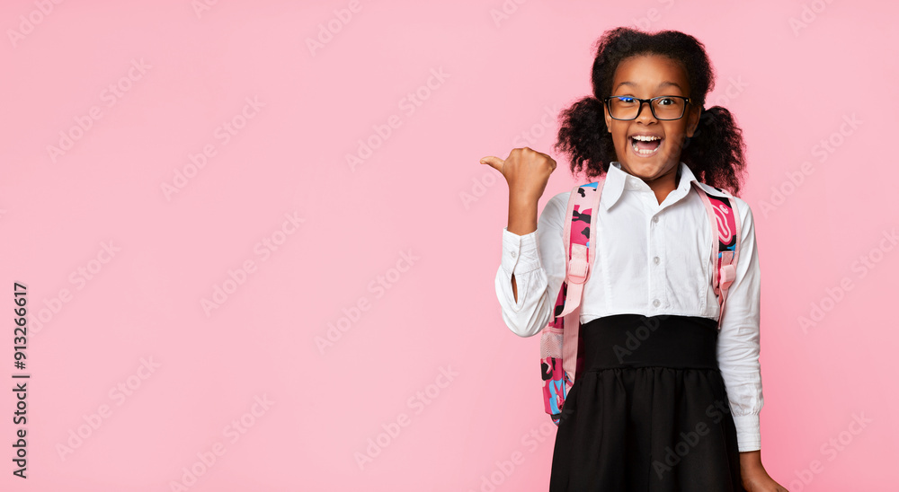 Wall mural Look There. Excited Afro Elementary Student Girl Pointing Thumbs At Copy Space Over Yellow Studio Background. Panorama