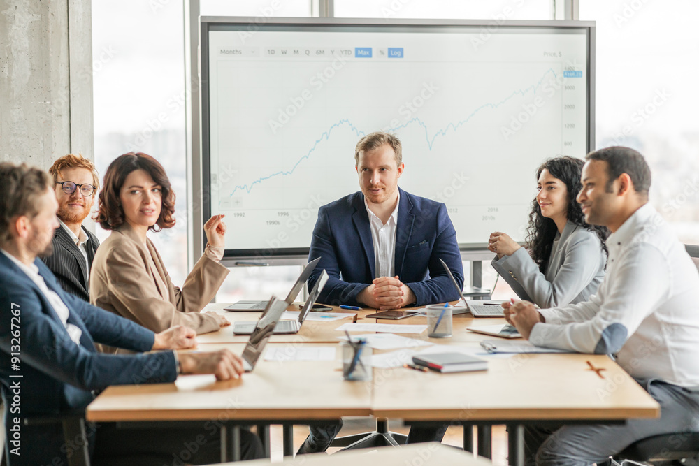Fototapete A group of business professionals are gathered around a table in a modern office, discussing a growth chart displayed on a large screen. The team is engaged in a lively conversation