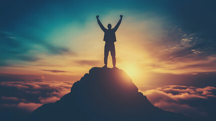 Silhouetted figure with raised arms standing triumphantly atop mountain peak against dramatic sunset sky with clouds, copy space