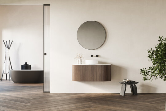 Interior of modern bathroom with white walls, wooden floor, bathtub, dry plants, white sink standing on wooden countertop and a oval mirror hanging above it.