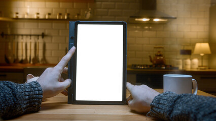 Point of view shot: Close-up of man using white mock-up screen digital tablet computer on the table. Man scrolls and taps on tablet computer in modern kitchen background.	
