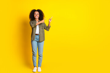 Full size photo of lovely girl with perming coiffure wear khaki shirt directing at sale empty space isolated on yellow color background