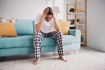 Obraz premium Photo of stressed depressed guy nightwear pajama having headache sitting couch indoors room home house