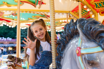 Happy emotional child riding on a merry go round at amusement park. Little girl playing on carousel, summer fun, happy childhood, vacation and entertainment concept