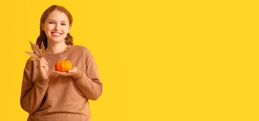 Pretty young woman holding pumpkin and autumn leaf on yellow background with space for text