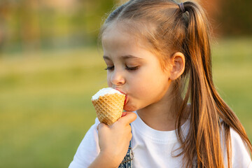 A happy laughing child in summer clothes eats ice cream on a hot day in park. Ice cream in a waffle...