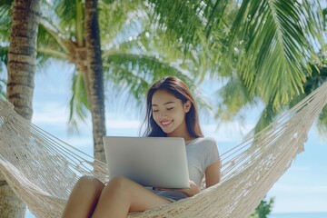 African American woman working on a laptop in a hammock by the tropical beach, palm trees and turquoise sea in the background. Remote work concept.