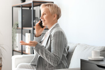 Mature businesswoman talking by phone while sitting on sofa in office