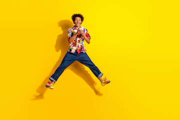 Full size photo of nice young man jump use phone wear shirt isolated on bright yellow color background