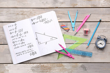 Copybook with maths formulas and stationery on grey wooden background