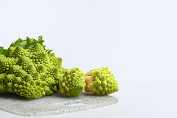 Board with fresh Romanesco broccoli on light background