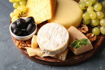 Plate with different types of tasty cheese and grapes on green background, closeup