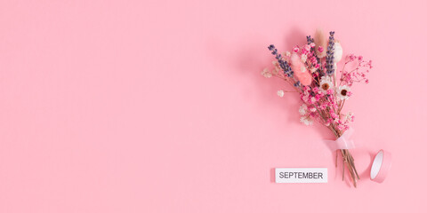 September - word on wooden block, beautiful bouquet of different dried flowers on pastel pink...