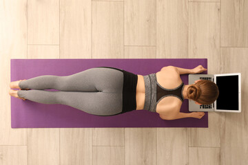 Sporty young woman with laptop doing yoga in gym, top view