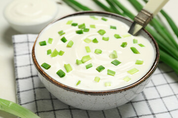 Bowl of tasty sour cream with green onion on table, closeup