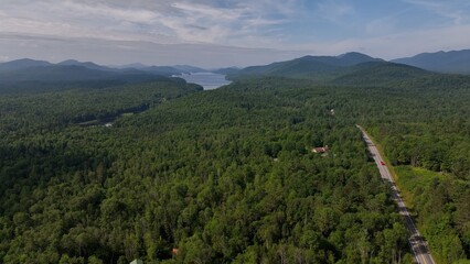 Traveling in Adirondack Mountains past lakes, mountains, green trees under blue sky with clouds on summer vacation to hike and camp in peaceful mountains in New York State forest