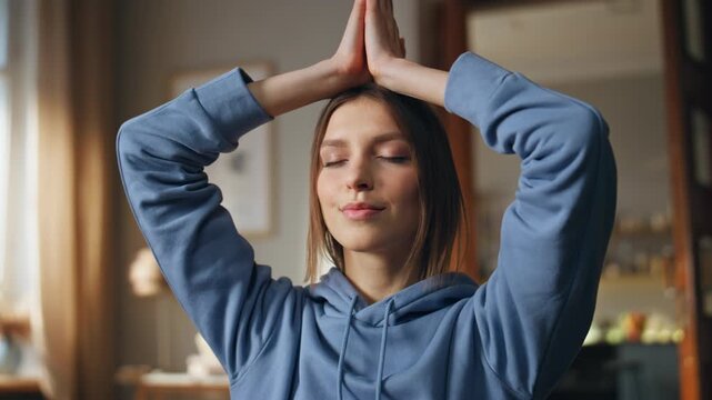 Woman making namaste hands meditating in lotus pose at home couch closeup.