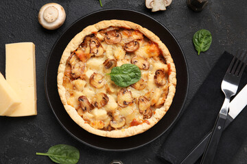Mushroom pie with spinach leaves and cutlery on black grunge table