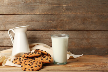 Tasty cookies with chocolate chips and glass of milk on wooden background