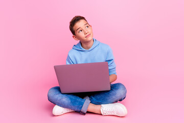 Full length photo of charming teen boy sit floor netbook look empty space dressed stylish blue garment isolated on pink color background