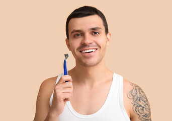 Handsome young man with razor on beige background