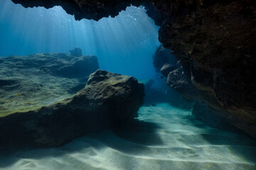 An underwater scenic view from inside a cave as the sun penetrates the water, raining sun rays down...