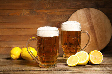 Glasses of fresh beer with lemons on wooden background