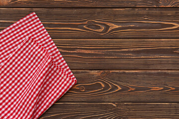 Obraz premium Red and white gingham checkered fabric napkin on dark brown rustic wooden table background, the textile provides a classic country or farmhouse aesthetic for dining and kitchen concepts