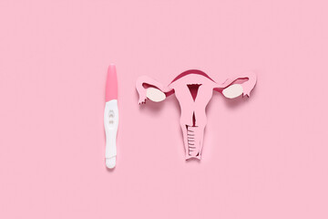 Paper uterus with pregnancy test on pink background